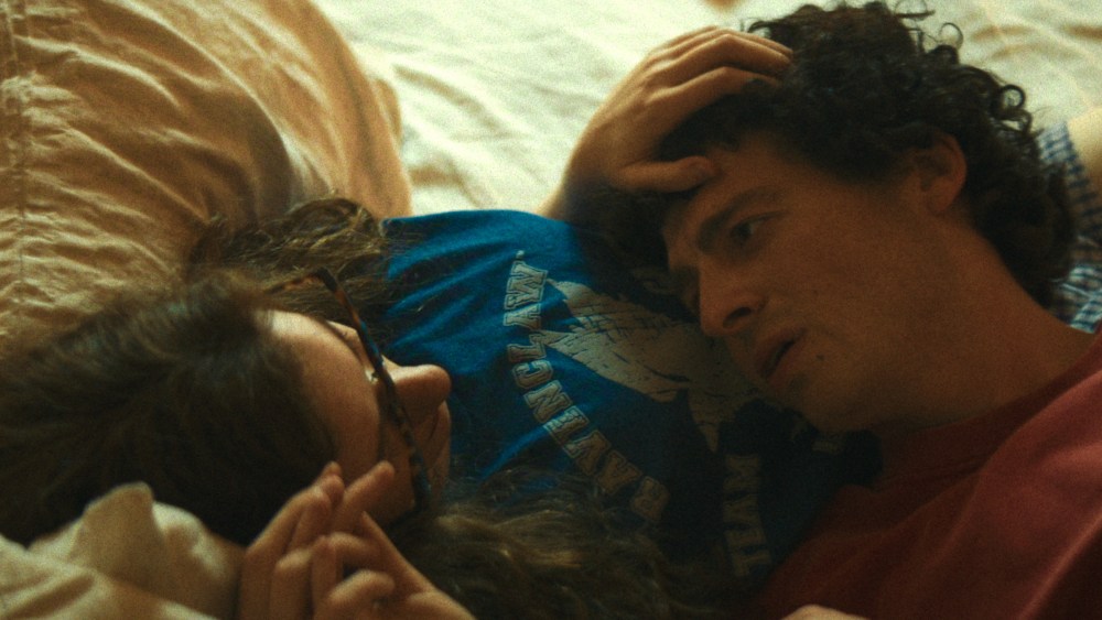 Anthony Boyle as Sam Bankman-Fried and Julia Garner as Caroline Ellison lying together on a bed in a still from The Altruists